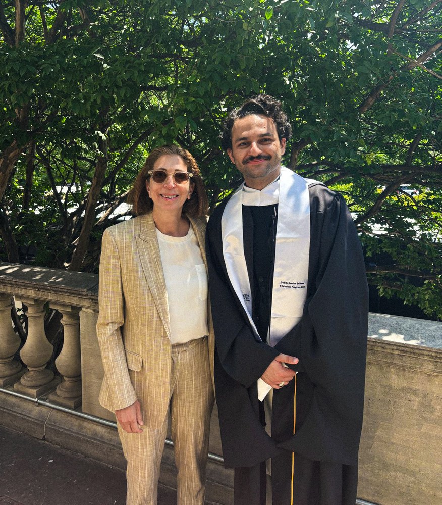 Umar Zafar in graduation robes standing with his mentor Lana outdoors.