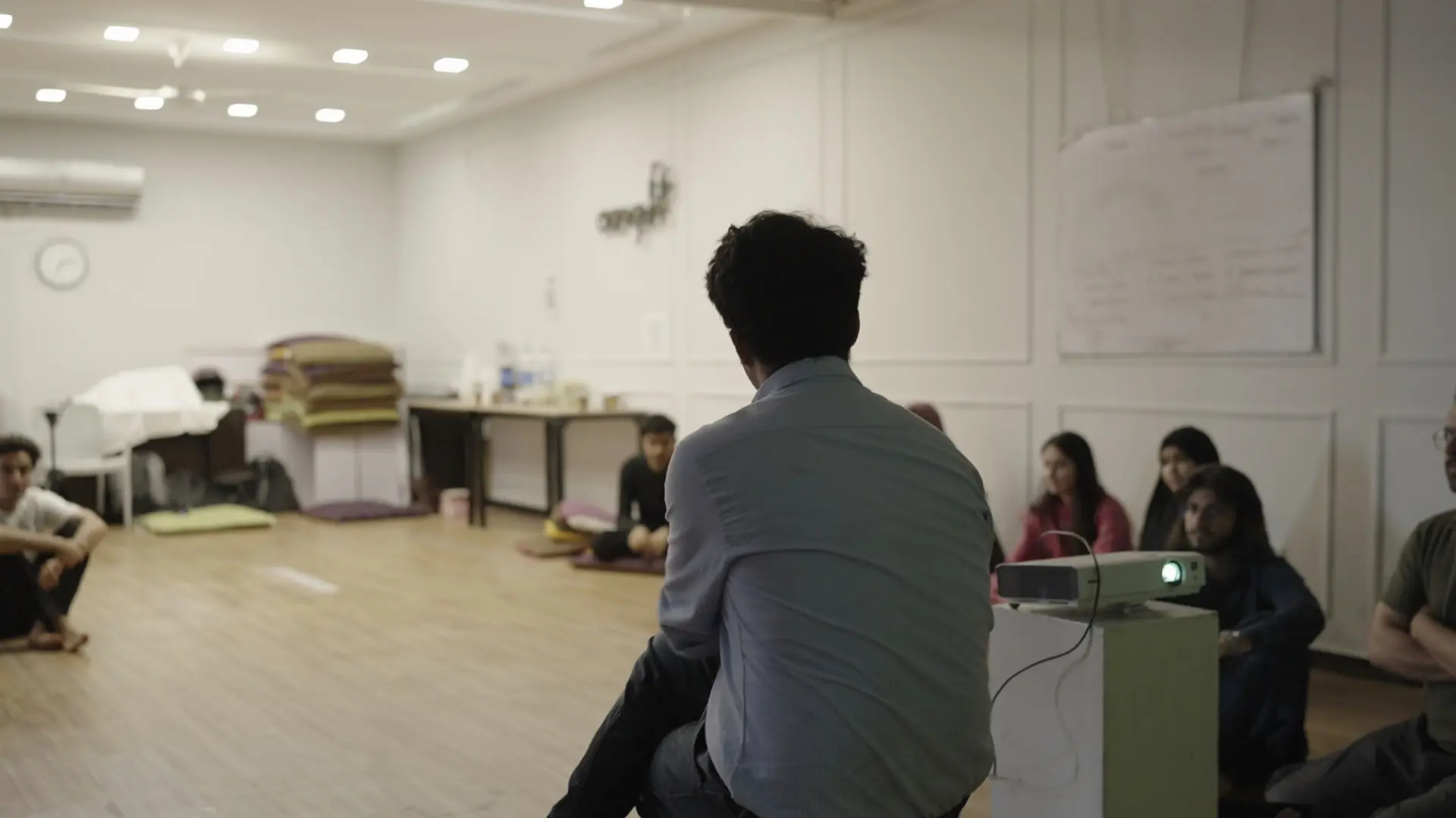 A facilitator addresses the cohort seated on floor cushions in the workshop hall