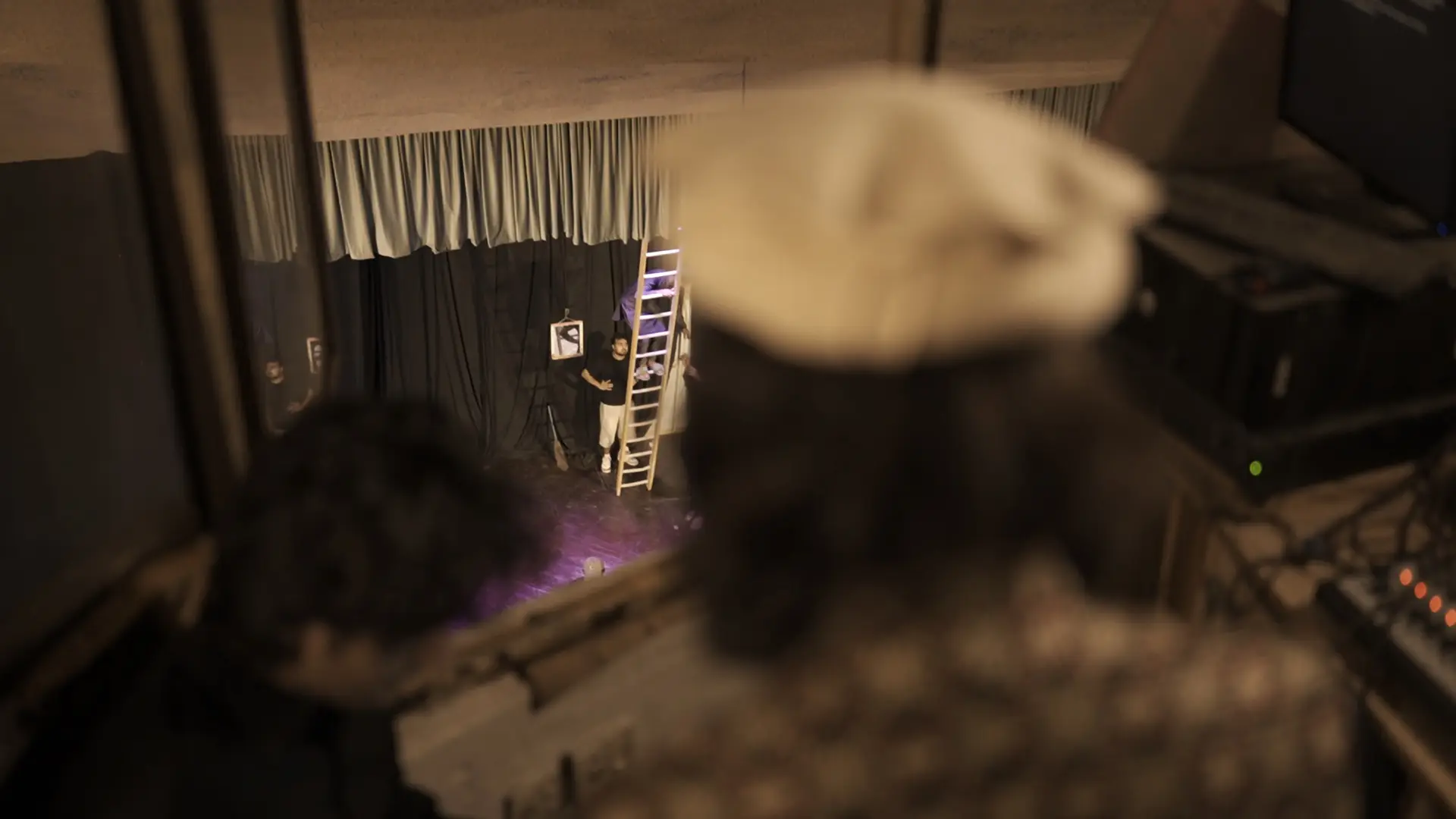 The performance seen from the wings, a performer on the ladder set piece in the distance