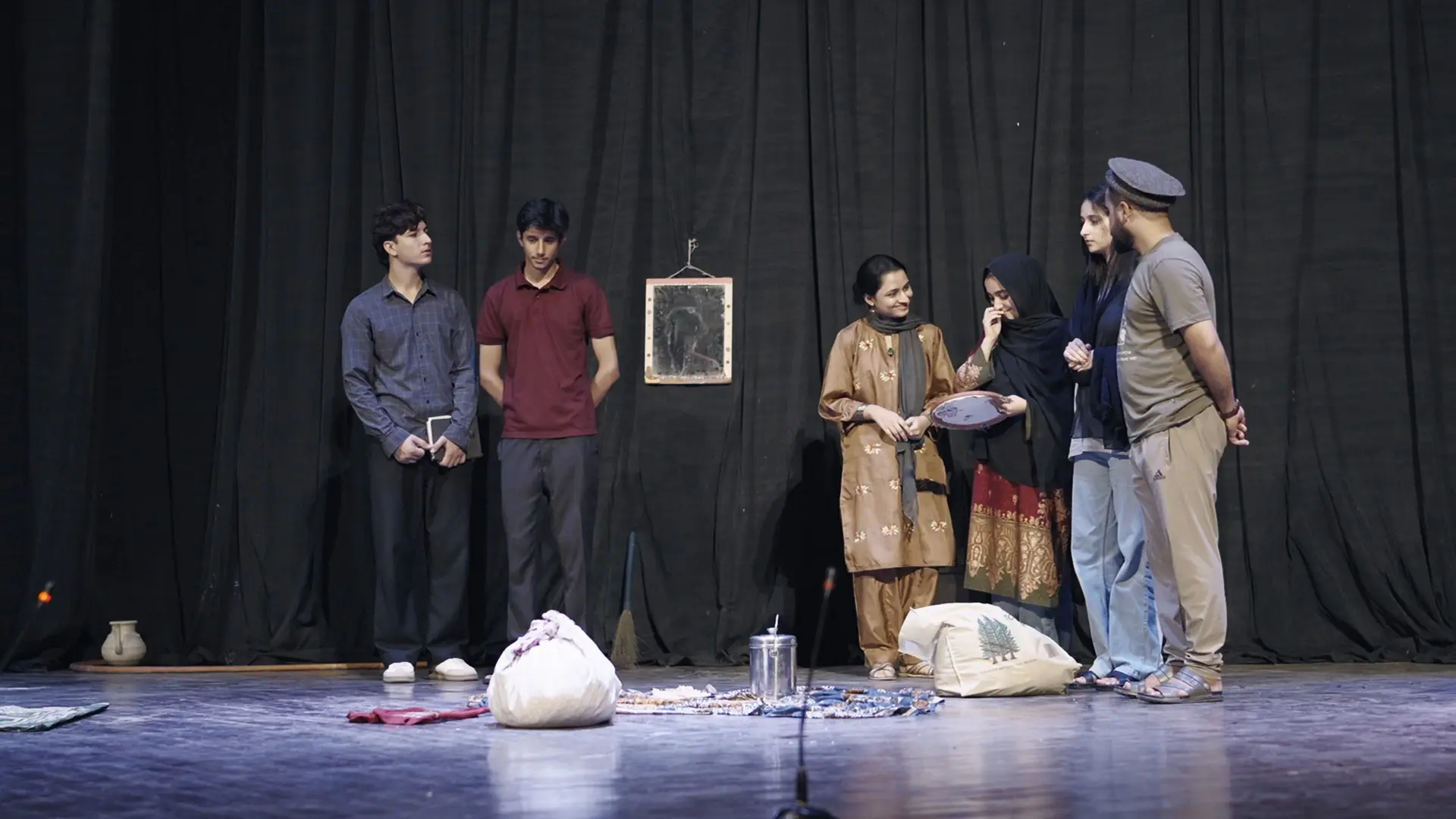 Participants perform a scene of Hate for Sale on the Alhamra stage, with household props at their feet